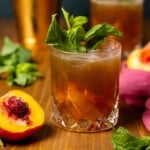 Mokctails in a glass with peaches, mint leaves, and a gold cocktail shaker.