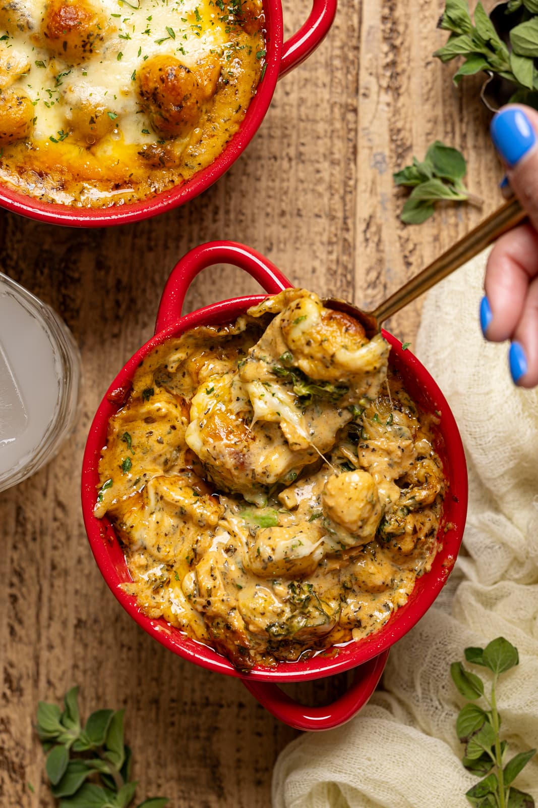 Baked gnocchi in a red bowl with a spoon lifted and cheese pulled. 