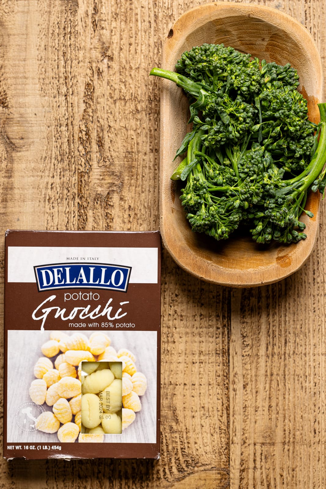 Package of gnocchi and broccoli on a brown wood table.