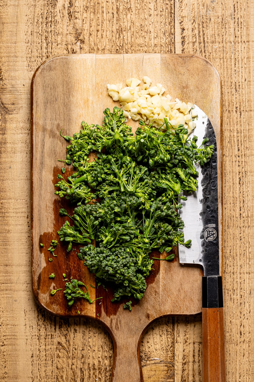 Chopped broccolini on a cutting board with a knife.
