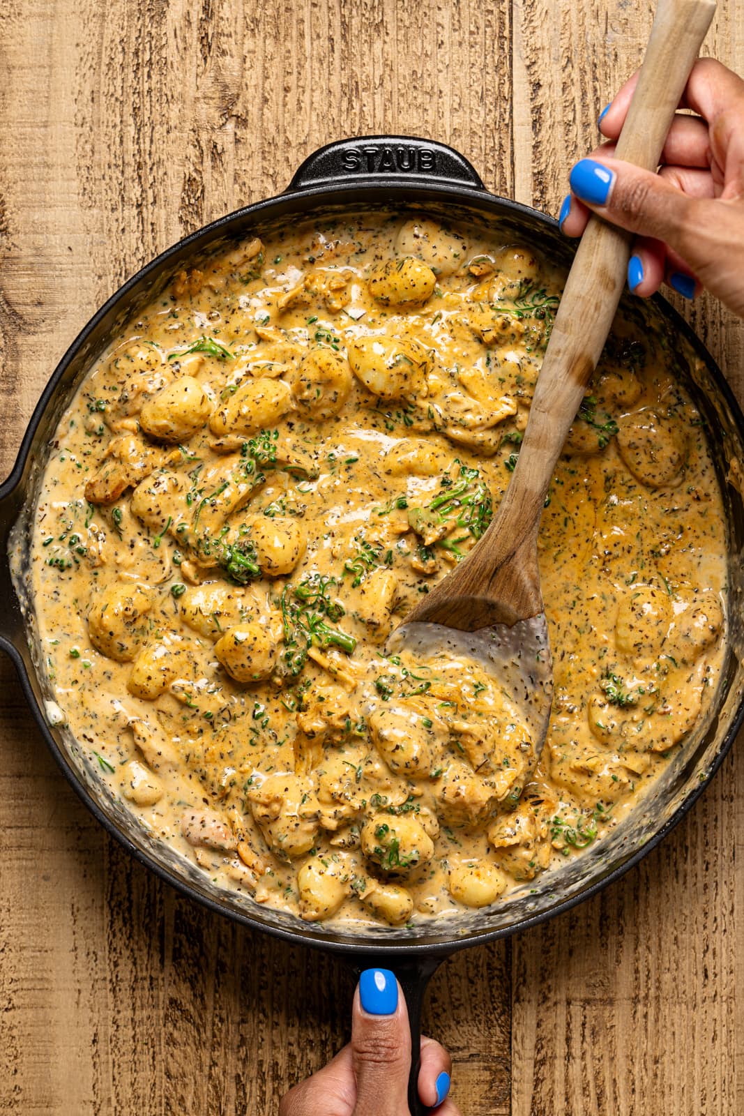 Gnocchi and chicken in a black skillet being held with a wooden spoon.