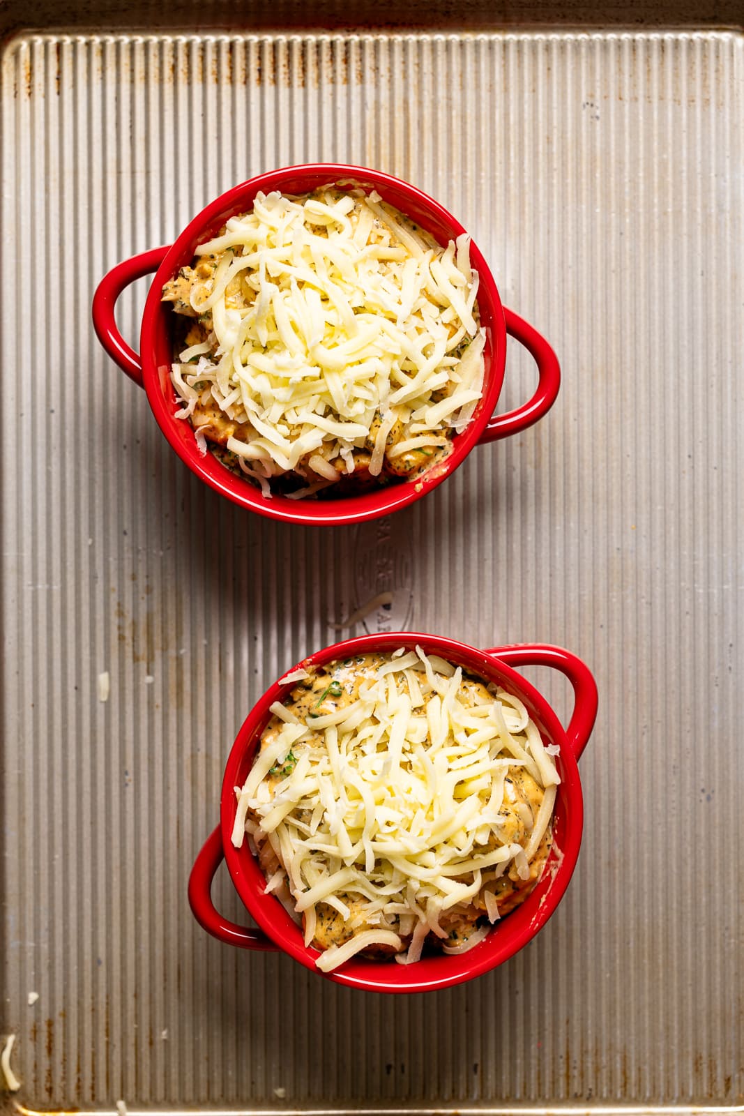 Everything in two small red bowls topped with shredded cheese on a baking sheet.