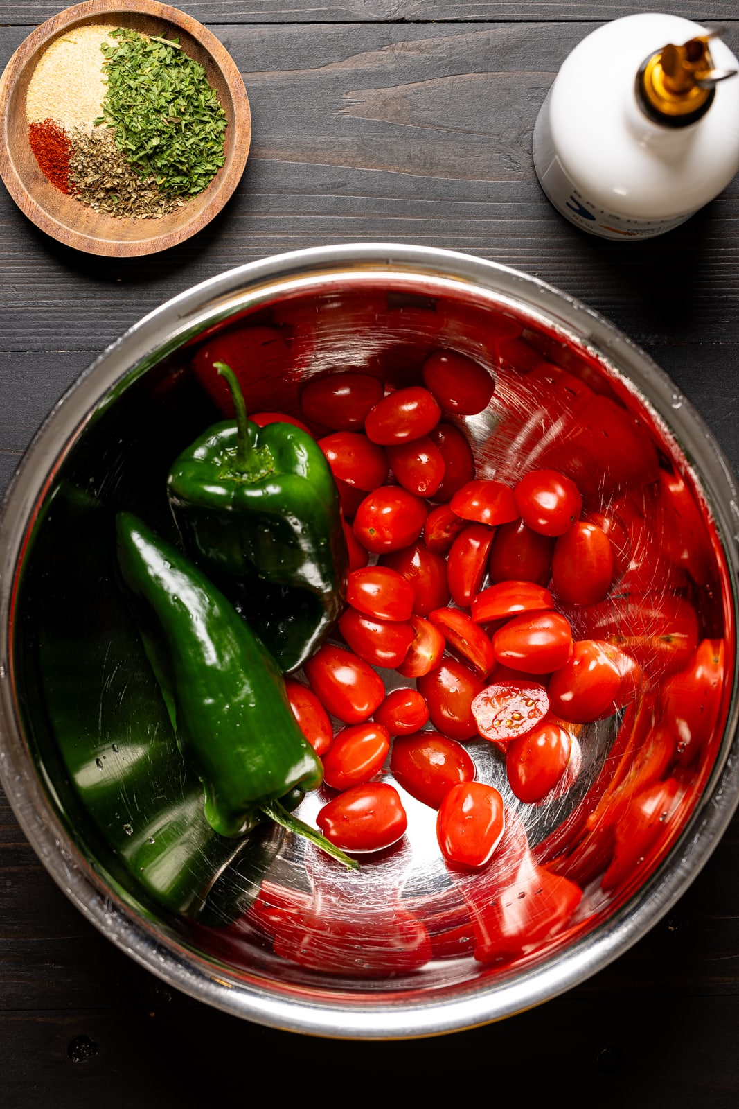 Tomatoes and peppers on a silver bowl with seasonings and olive oil.