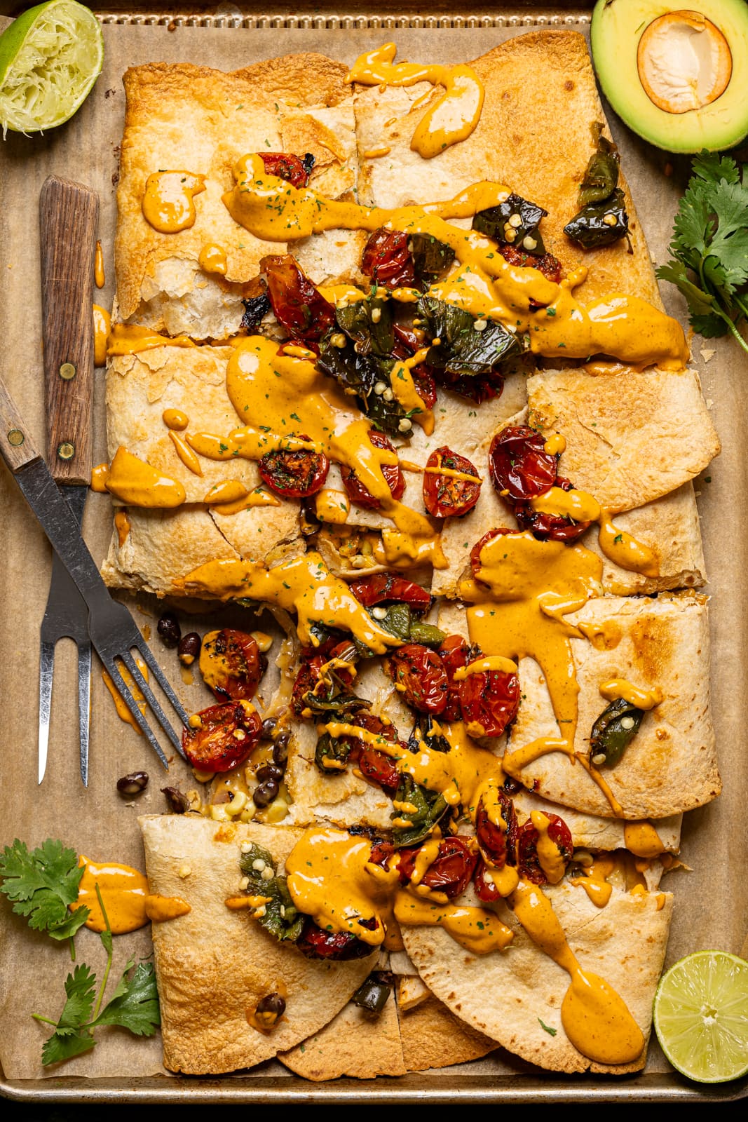 Quesadilla chopped on a baking sheet with toppings, chipotle, and two forks. 