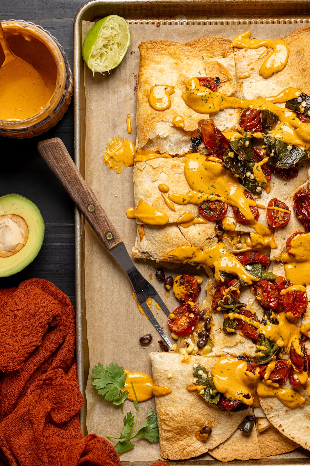 Close up on quesadilla on baking sheet with fork, side of chipotle sauce, and avocado. 