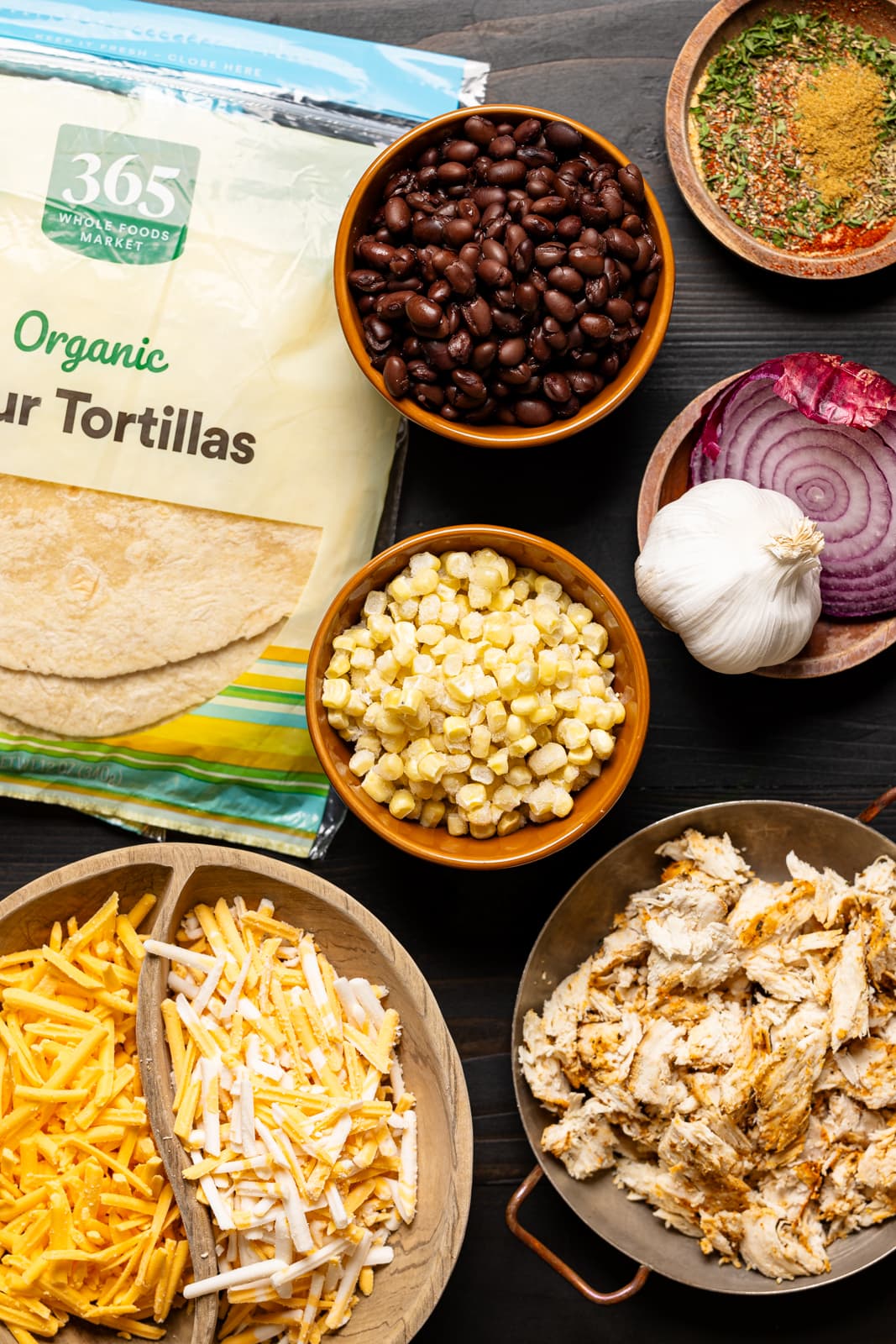 Ingredients including tortillas, corn, dairy-free cheeses, black beans, shredded chicken, and herbs + seasonings. 