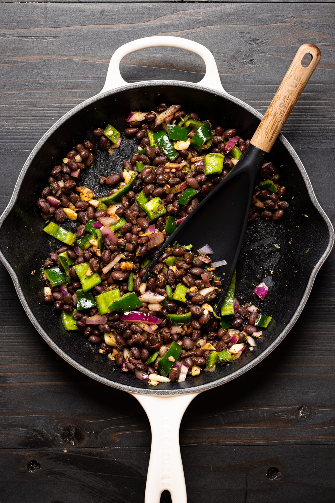 Black beans and veggies sautéed in a medium skillet with a spoon.