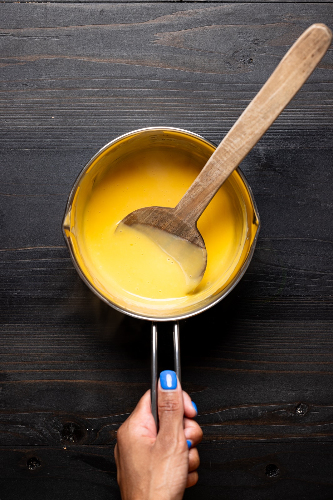 Melted dairy-free queso cheese in a saucepan with a wooden spoon.