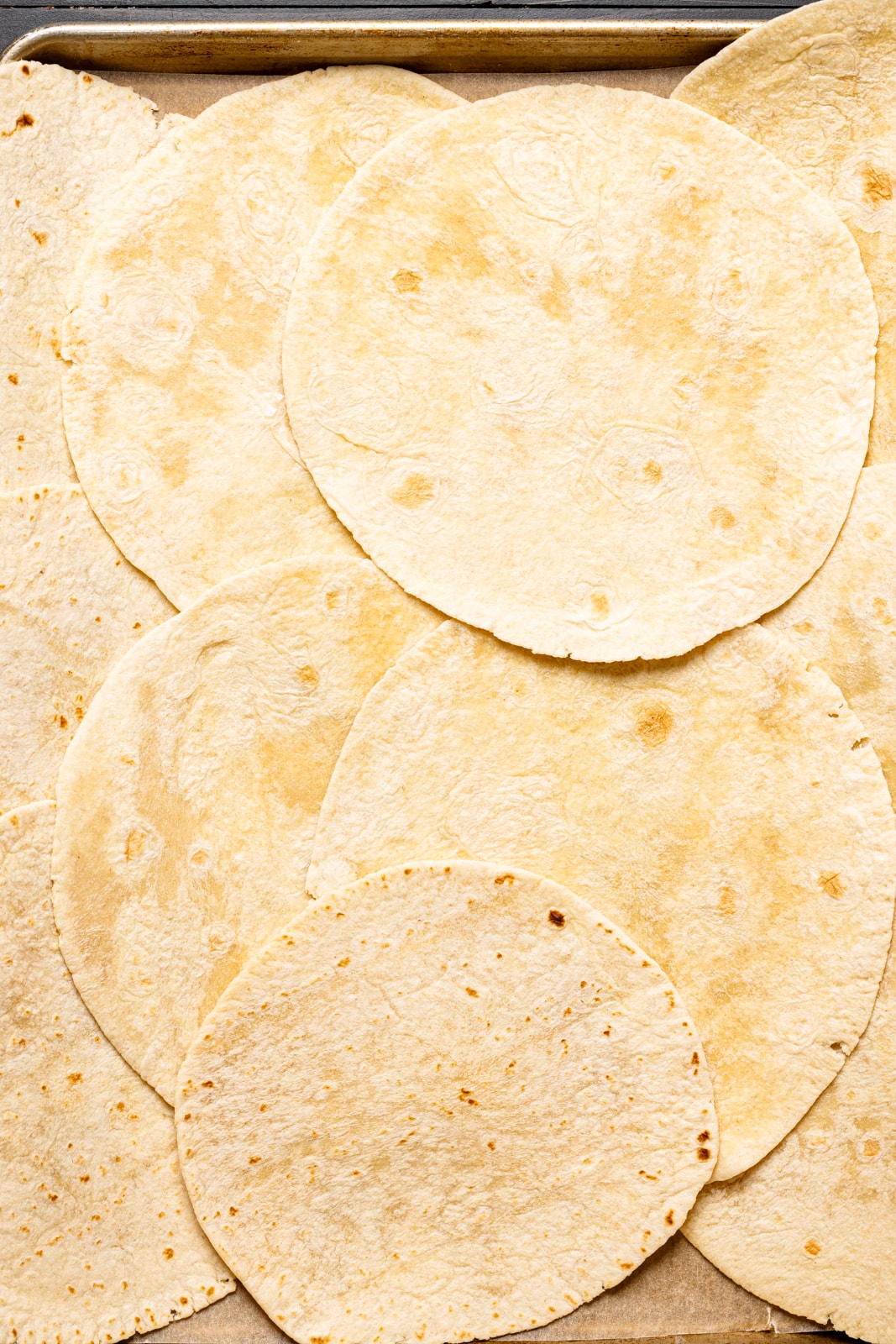 Flour tortillas lined unto a baking sheet, overlapping each other. 
