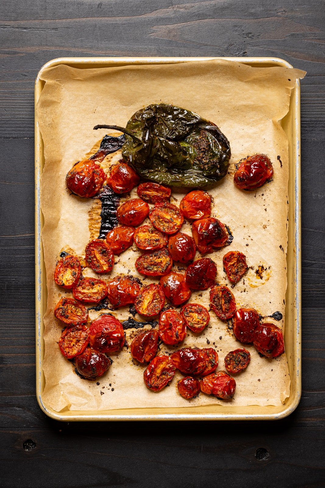 Roasted tomatoes and peppers on a baking sheet lined with parchment paper.