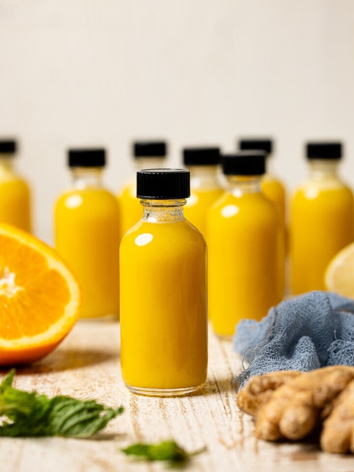 Juice in mini bottles on a white wood table with orange and ginger.