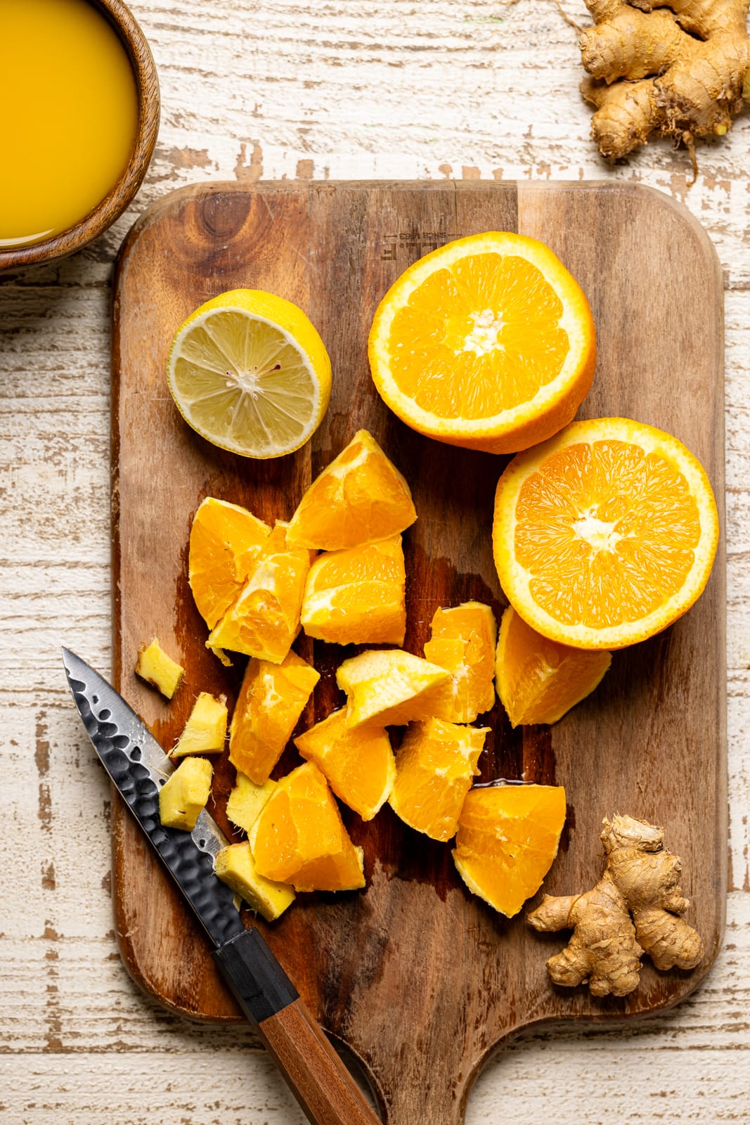 Ingredients for Detox Green Tea Shot Recipe. Sliced oranges, lemons, and ginger on a cutting board with a knife.