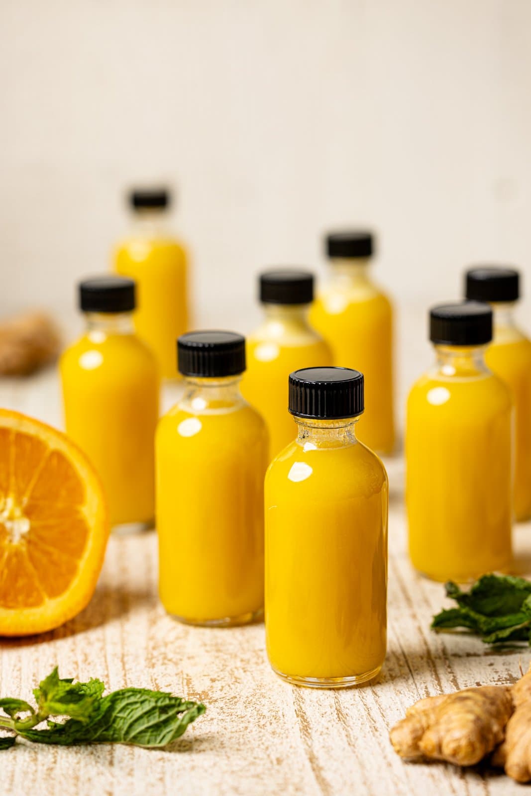 Mini bottles of juice lined next to each others with orange and ginger garnish.