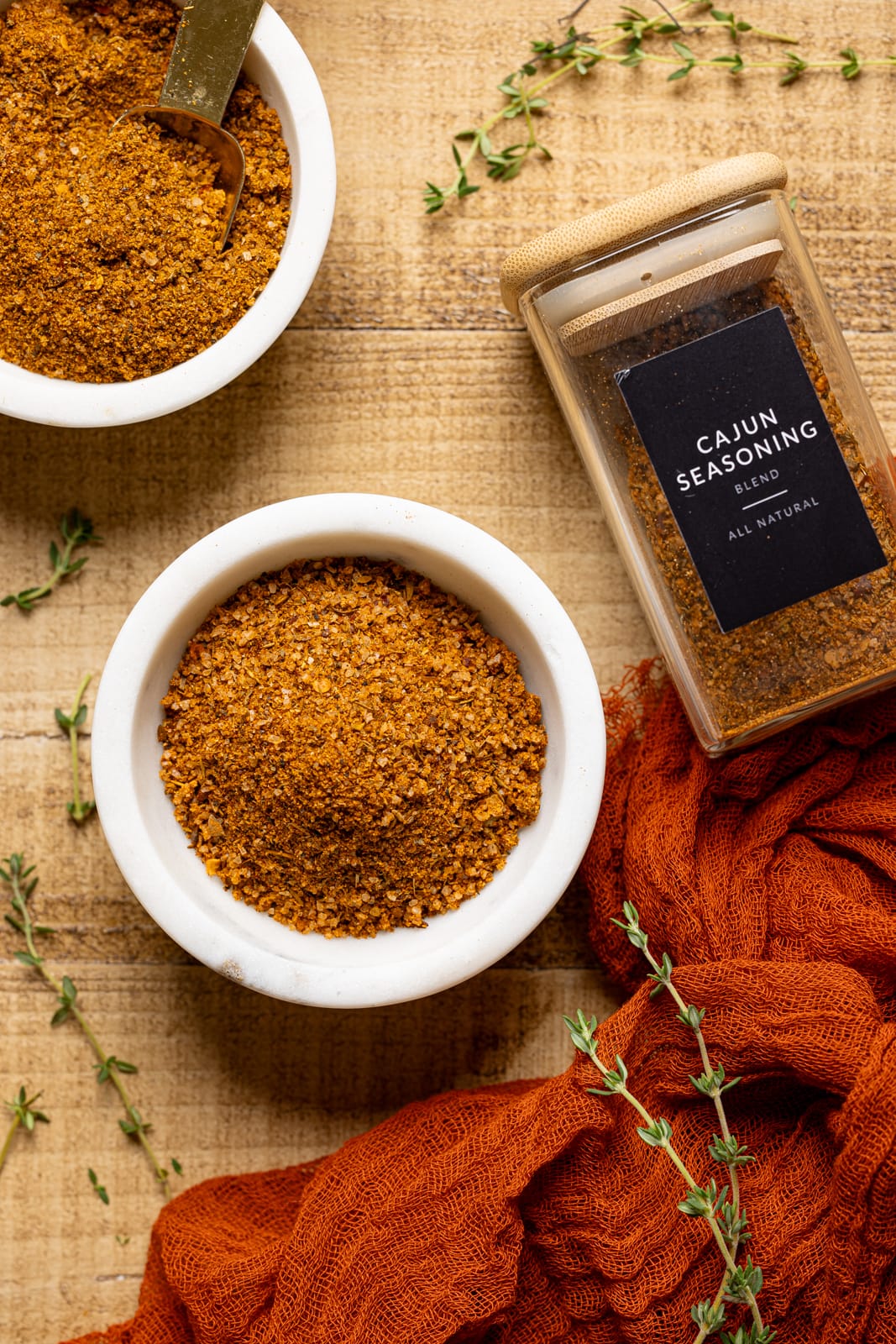 Cajun seasoning recipe ingredients in two white bowls with a red napkin and jar. 