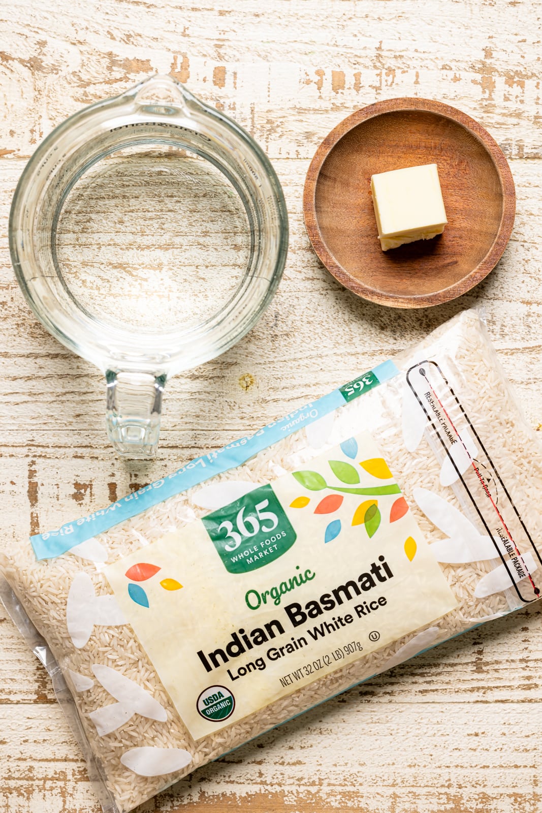 Ingredients on a white wood table including package of rice, water, and butter.