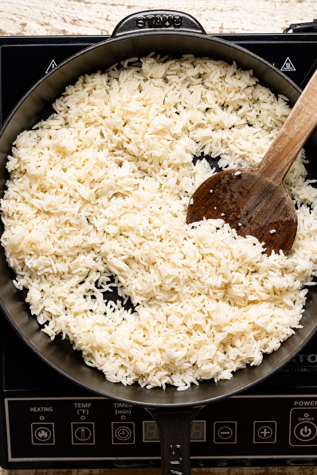 Cooked perfect basmati rice in black skillet with a wooden spoon.