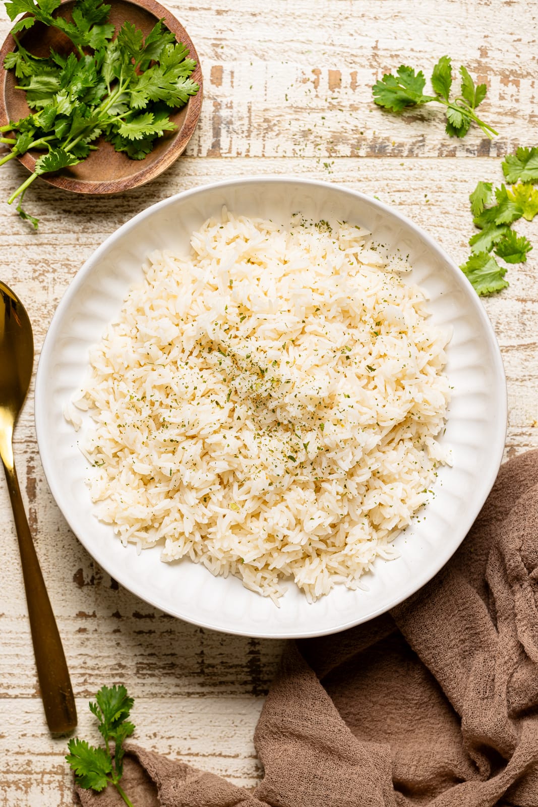 Cooked rice in a white bowl with a spoon, brown napkin, and herbs.