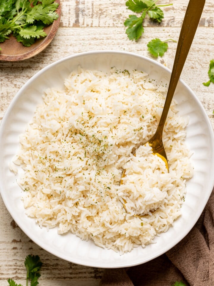 Cooked rice in a white bowl with a gold spoon with herbs.