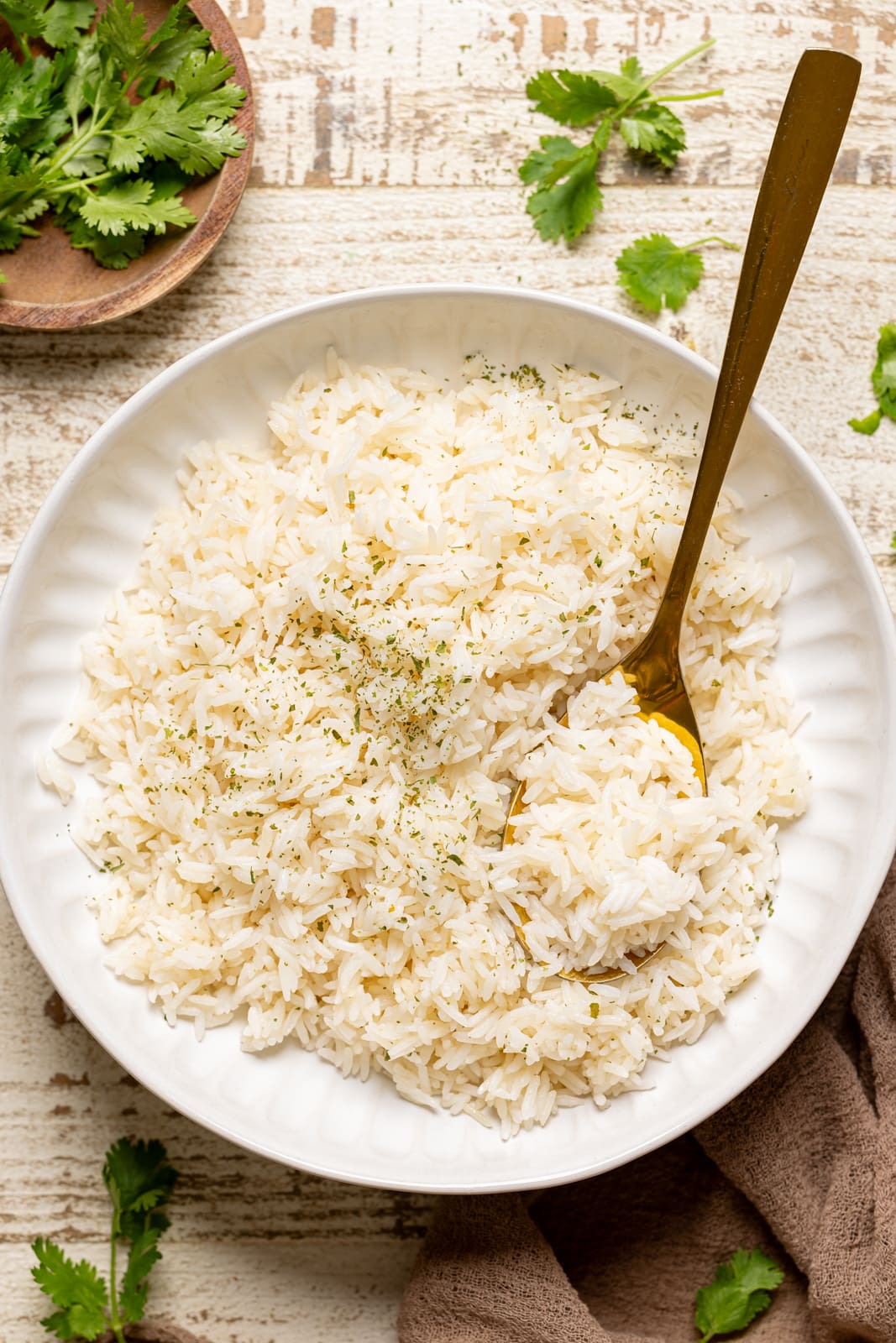 Cooked rice in a white bowl with a gold spoon with herbs.