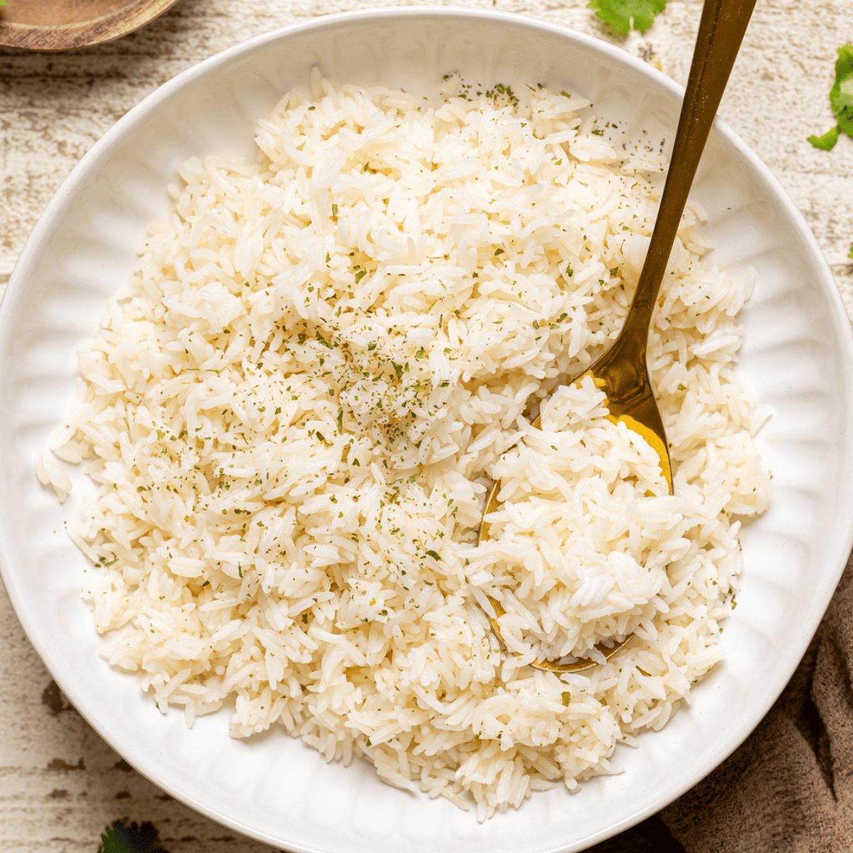 Cooked rice in a white bowl with a gold spoon with herbs.