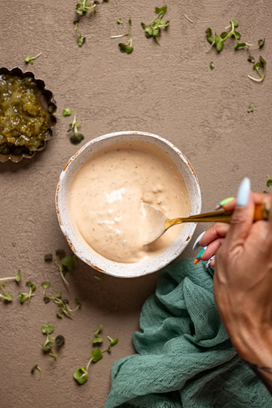 Sauce in a white bowl being stirred on a grey table.