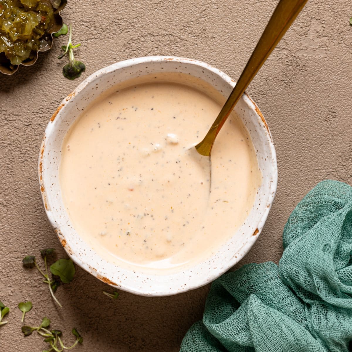 Sauce in a white bowl with a gold spoon and a side of radish.