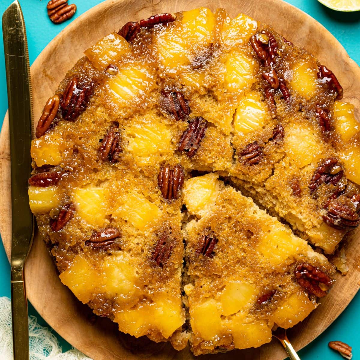 Cake sliced with a knife on a blue table with lime, pecans, and herbs.