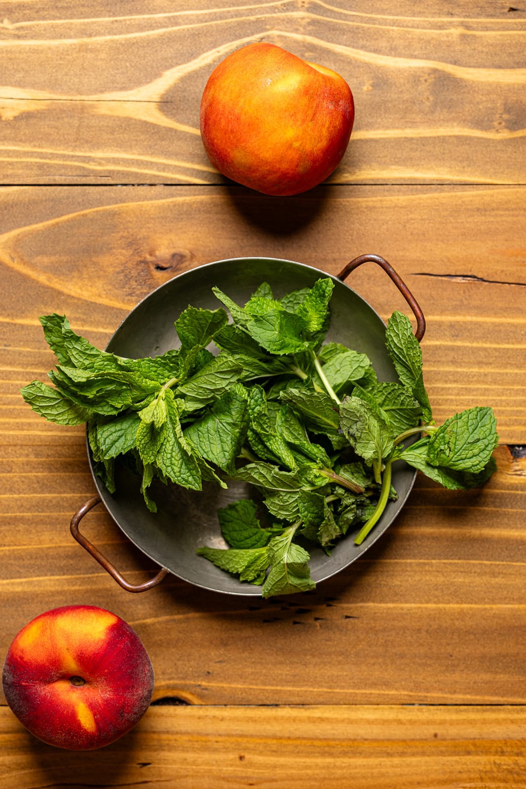 Mint leaves and peaches on a brown wood table.
