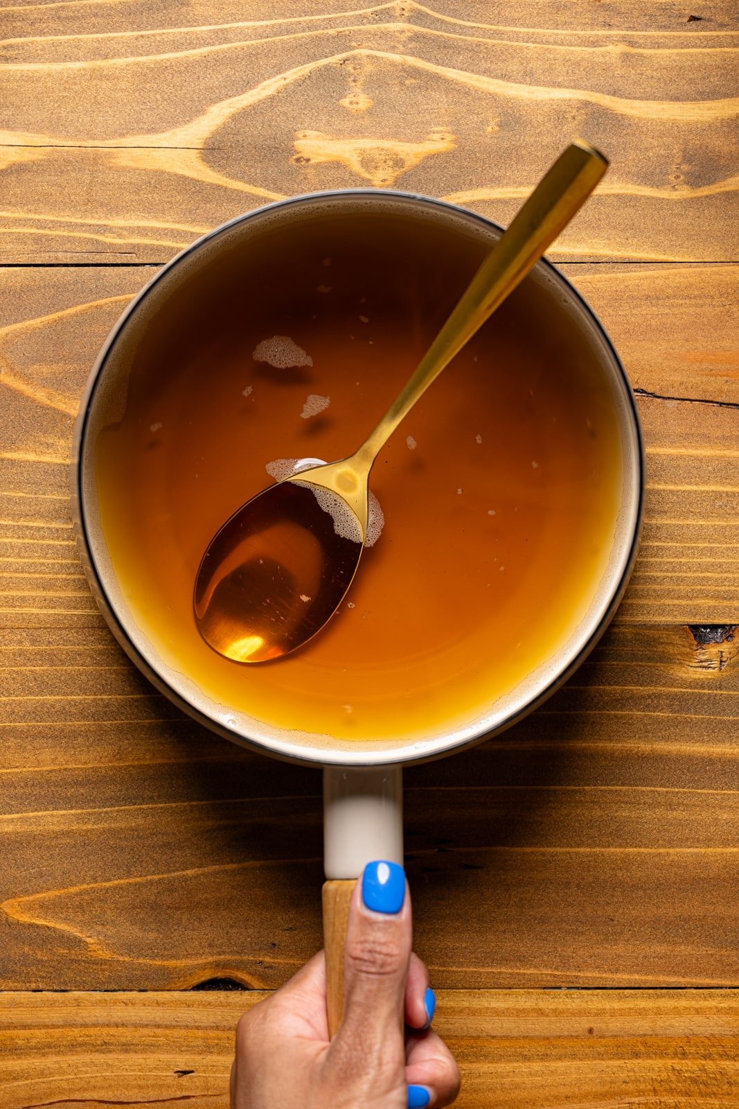Brown sugar syrup in a saucepan with a spoon being held. 