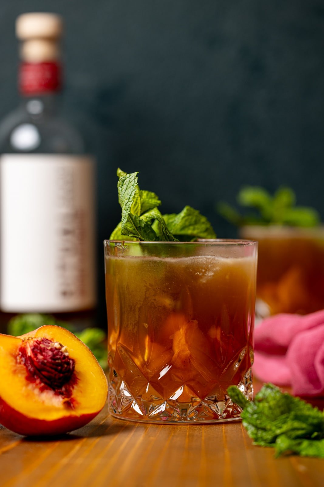 Mocktail in glasses with peaches, mint leaves, and bottle of alcohol alternative.