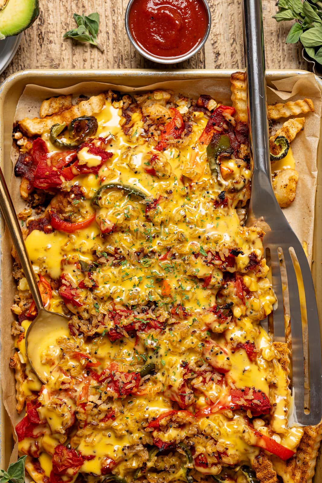 Nacho fries in a sheet pan with spatula and spoon with a side of ketchup. 