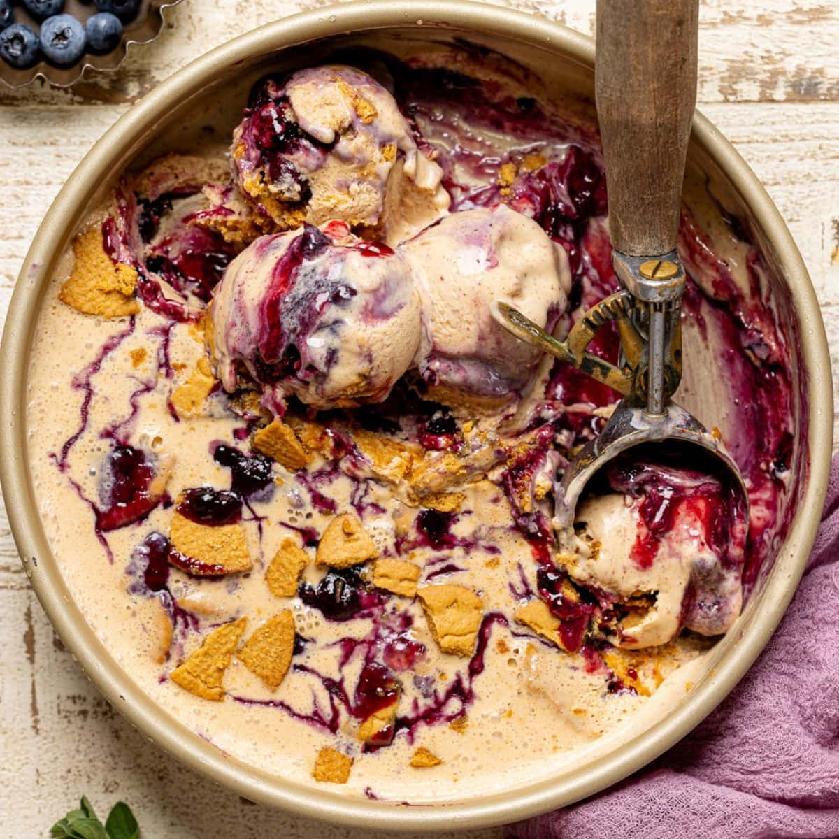 Scoops of ice cream in a round pan with a scoop and blueberries.