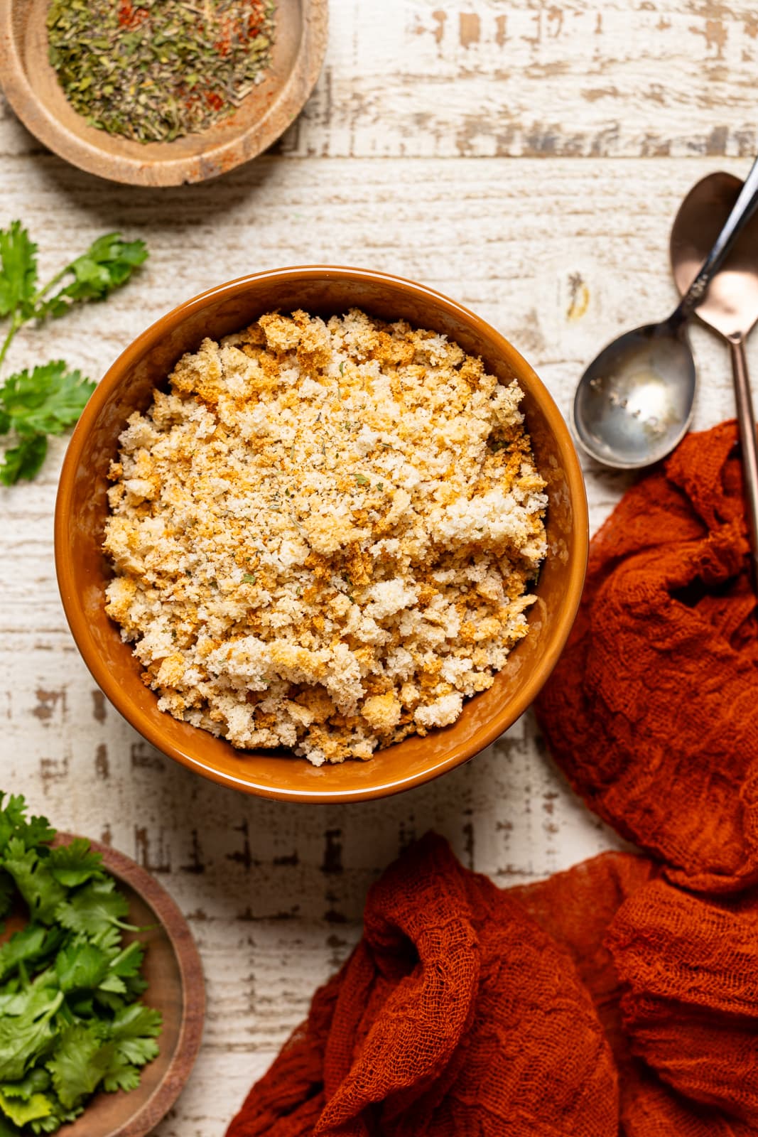 Bread crumbs in a bowl with spoons, a red napkin, and seasoning. 