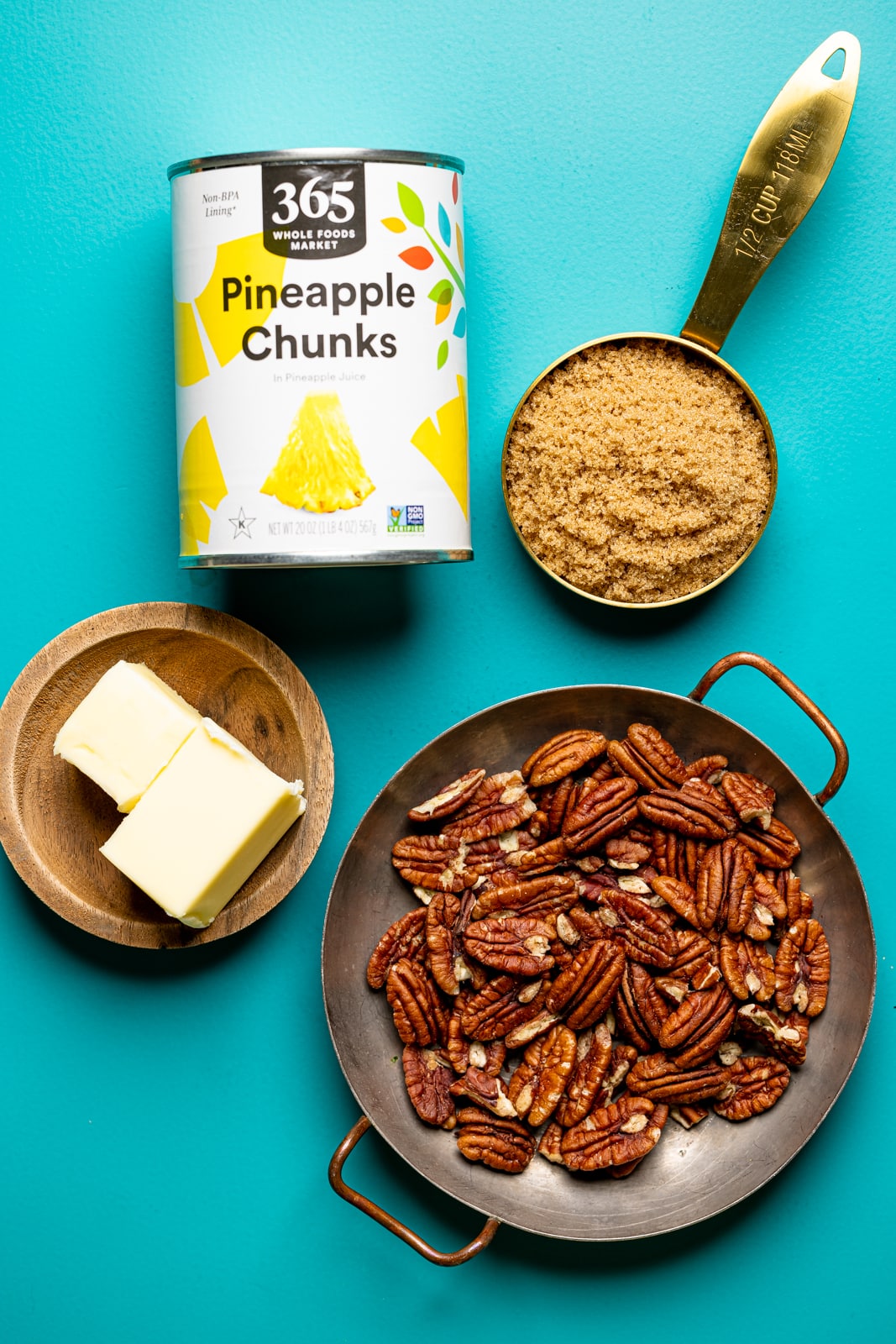 Ingredients for the topping on a blue table including pecans, butter, pineapples, and brown sugar. 