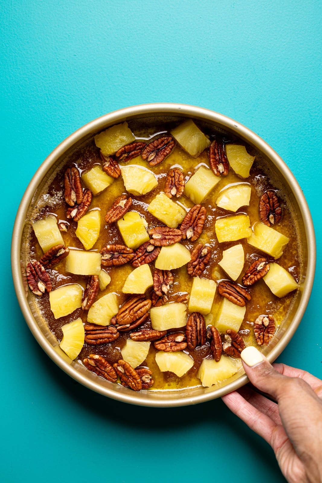 Pineapple and pecan topping in a round cake pan being held.
