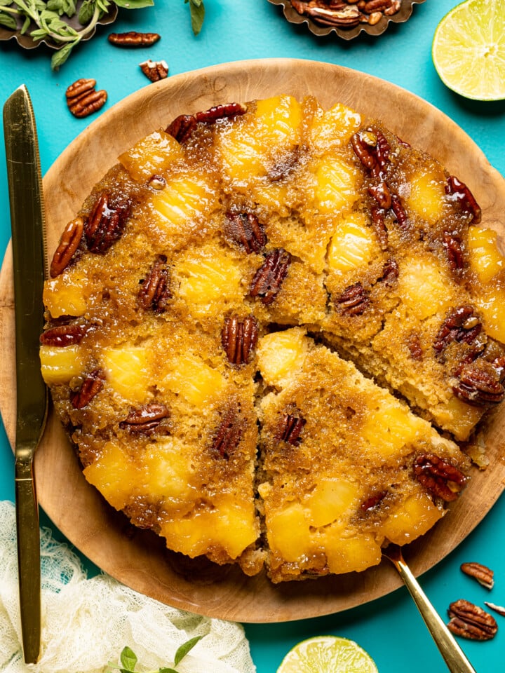 Cake sliced with a knife on a blue table with lime, pecans, and herbs.