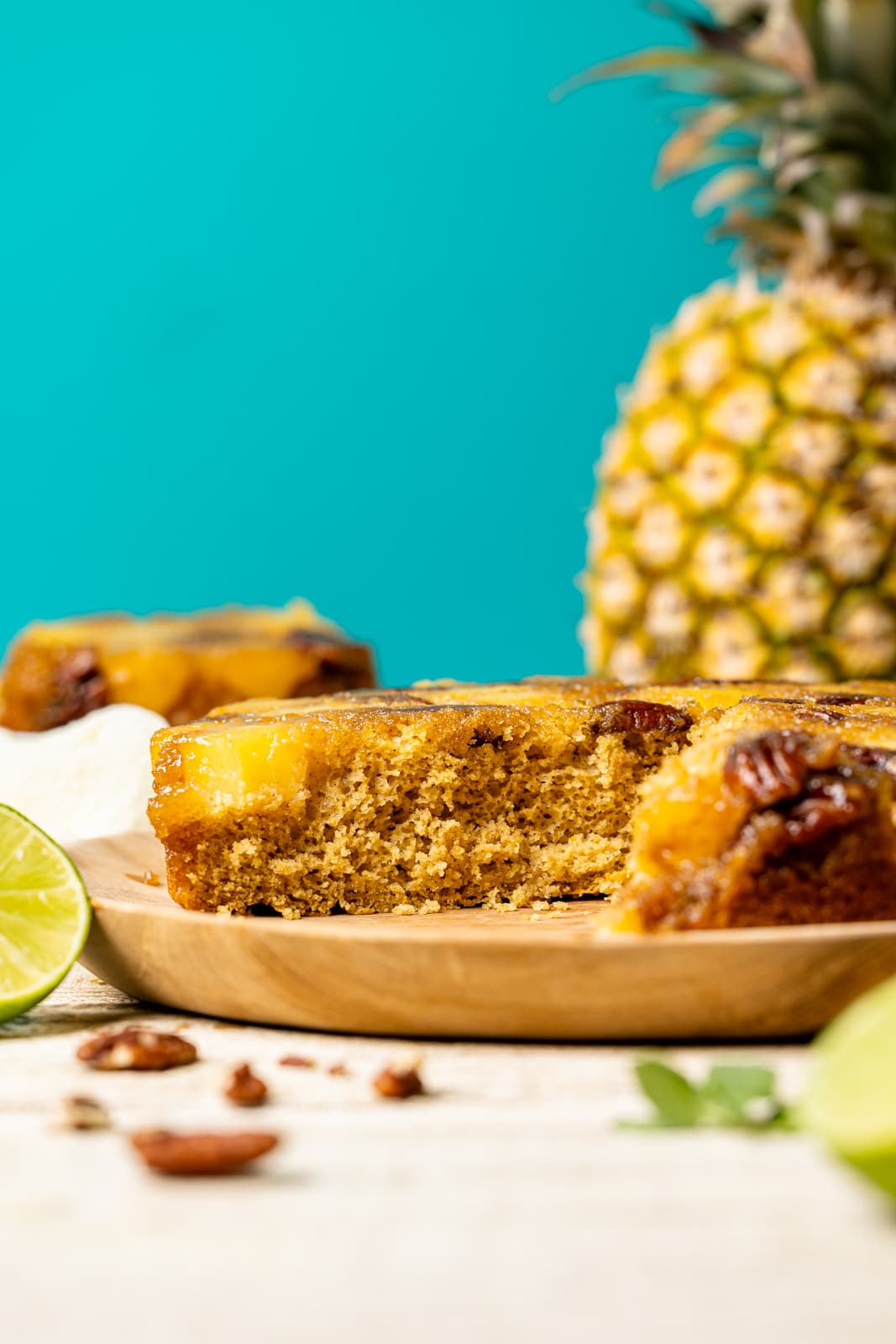 Forward view of cake with pineapple, lime, and pecans on a white table with a blue background.