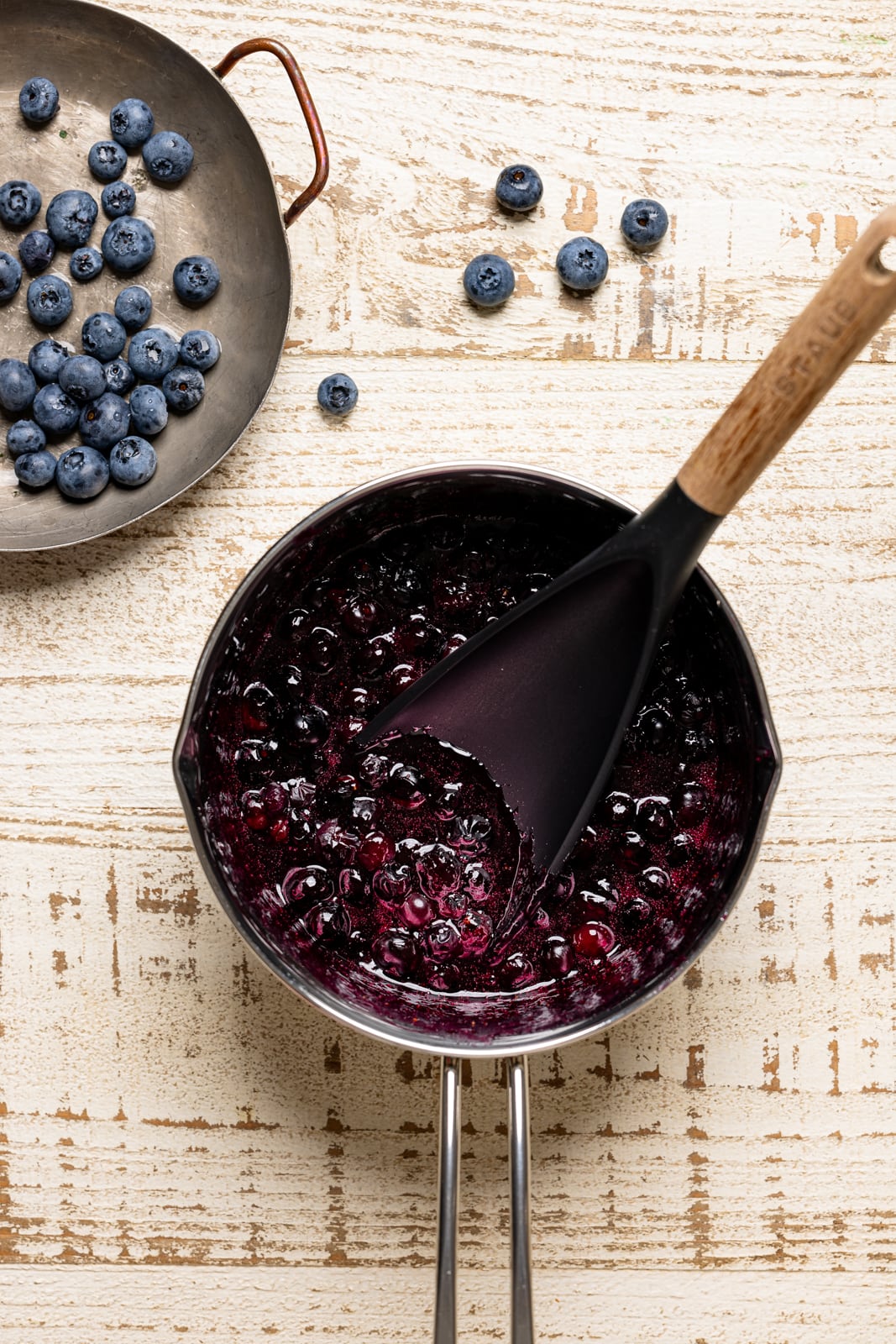 Blueberry compote in a saucepan with a spoon.