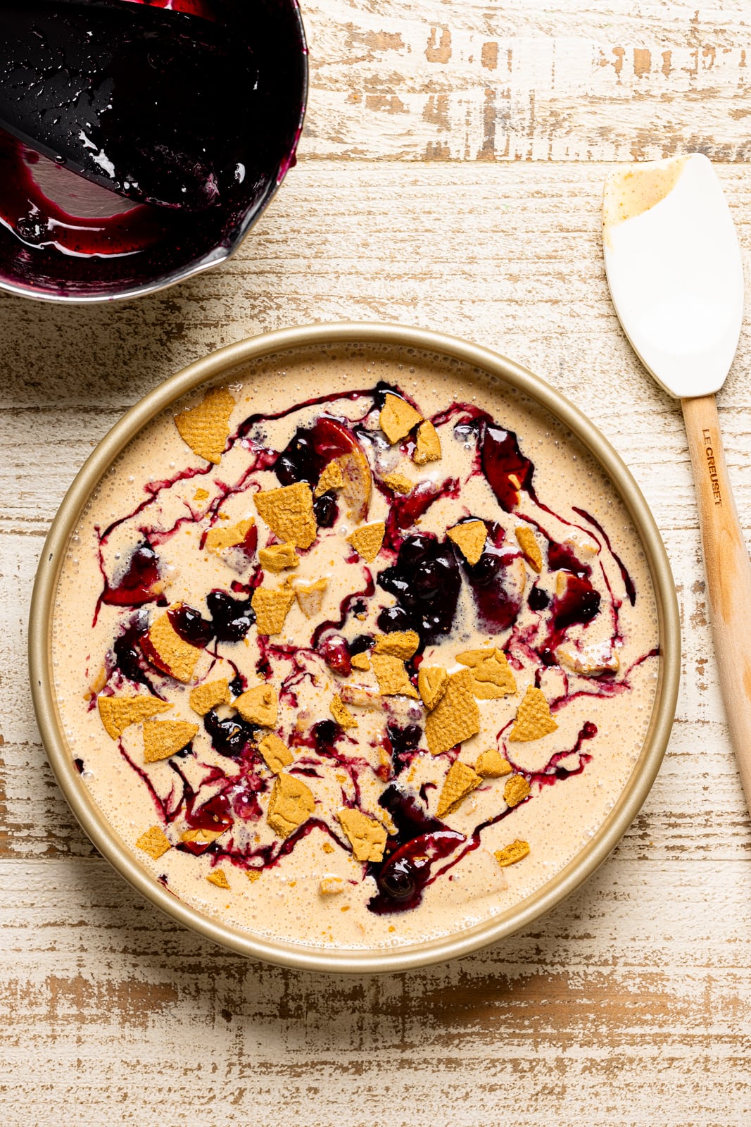 Ice cream in a round pan with blueberry compote and spatula. 