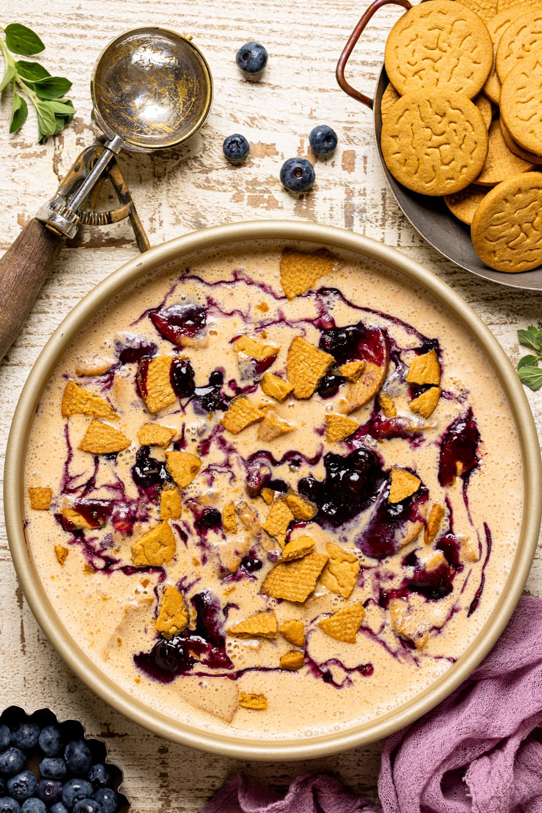 Up close shot of ice cream in a round pan with a scoop, gingersnap cookies, and blueberries. 