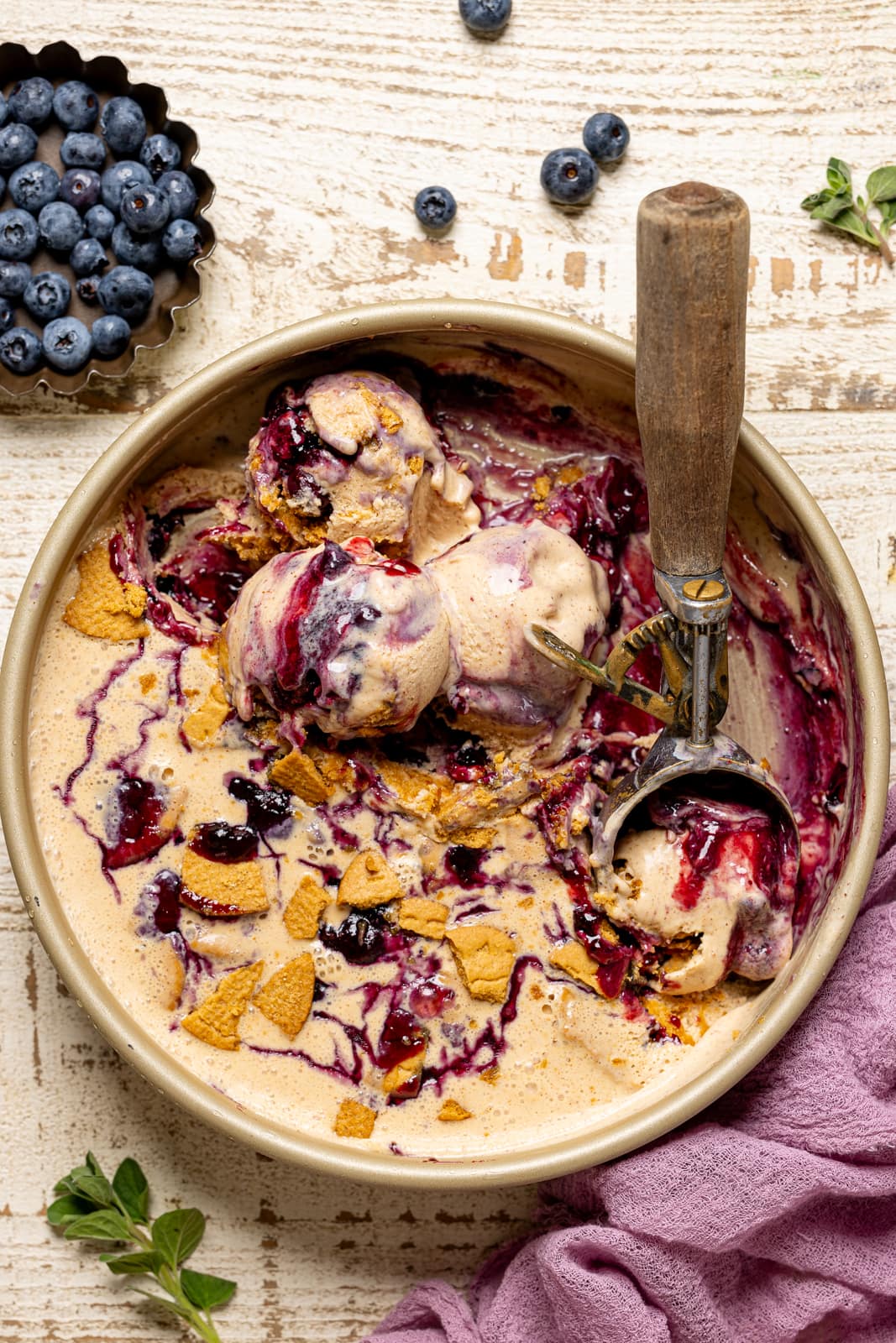 Scoops of ice cream in a round pan with a scoop and blueberries. 