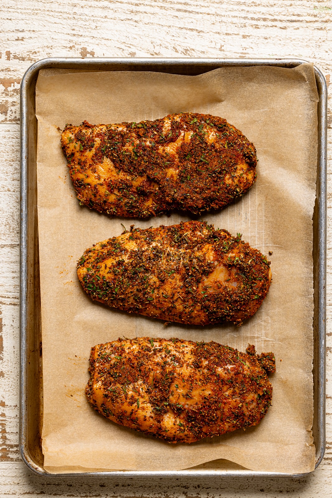 Seasoned chicken on a baking sheet with parchment paper lined side by side. 