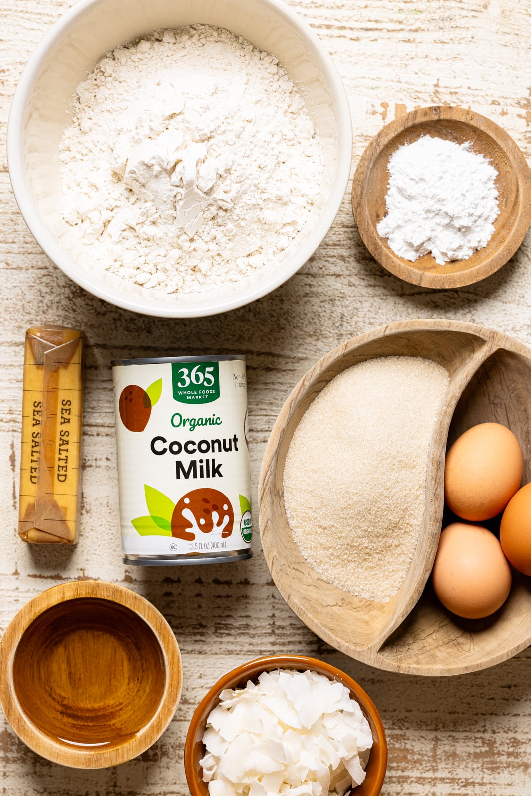 Ingredients including flour, eggs, sugar, coconut flakes, butter, coconut milk, and dry ingredients. 