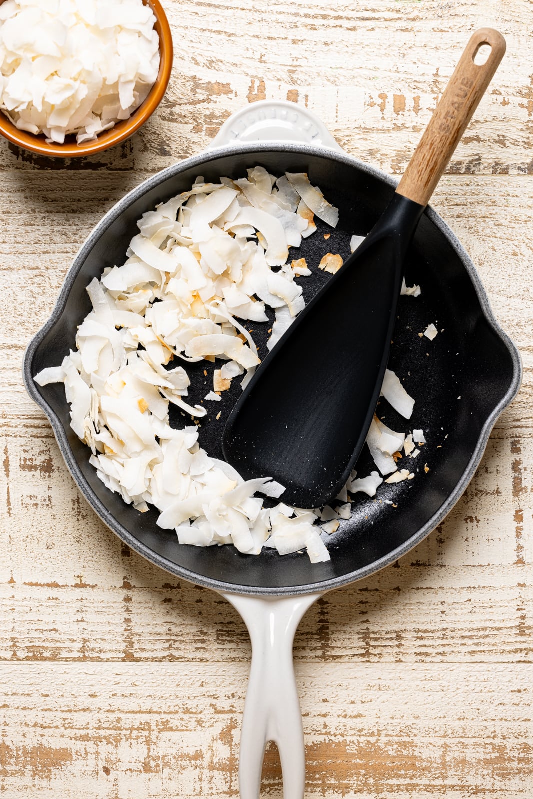 Toasted coconut flakes in a white skillet and spoon.