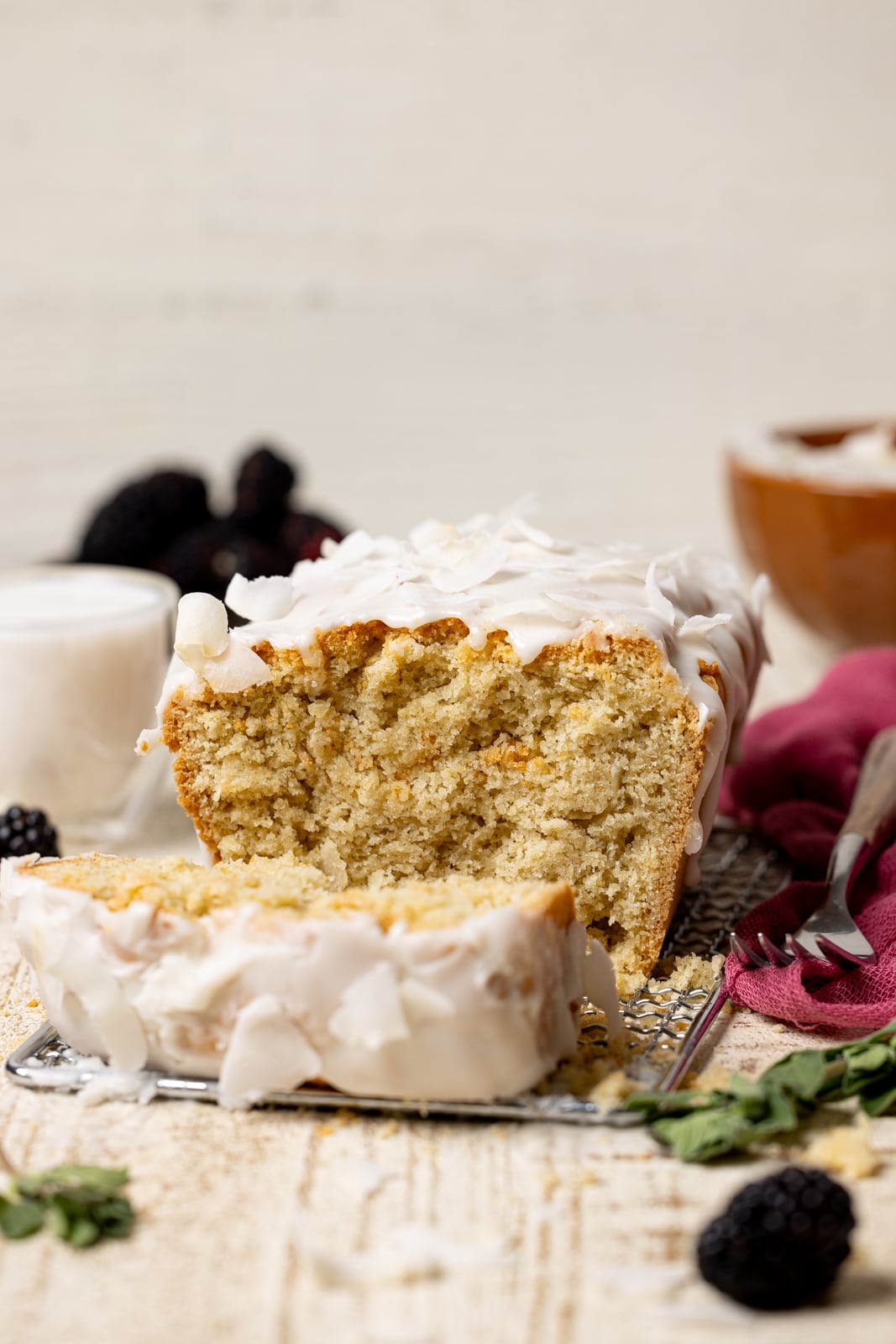 Sliced coconut bread with a fork, glass of milk, and blackberries. 