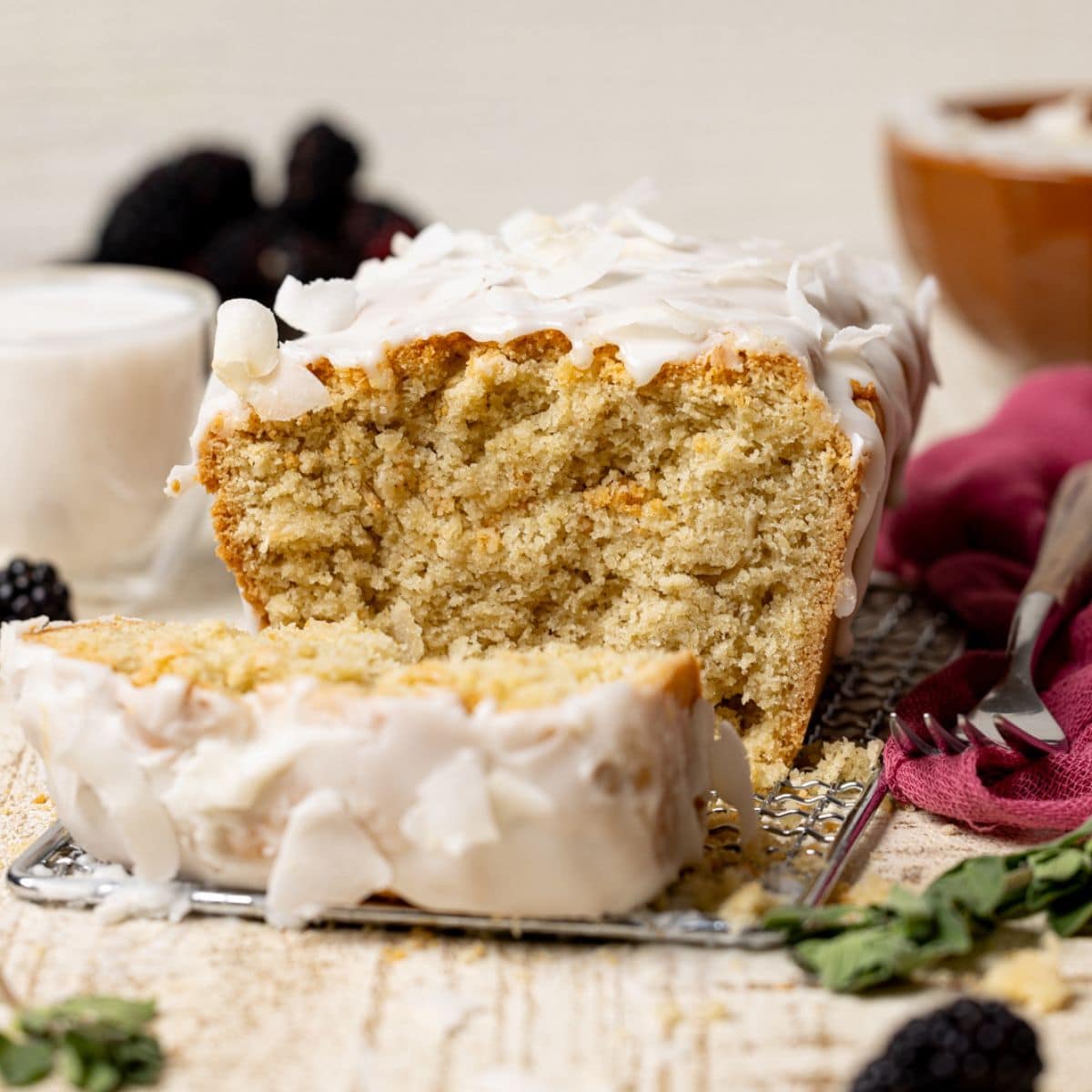 Sliced coconut bread with a fork, glass of milk, and blackberries.