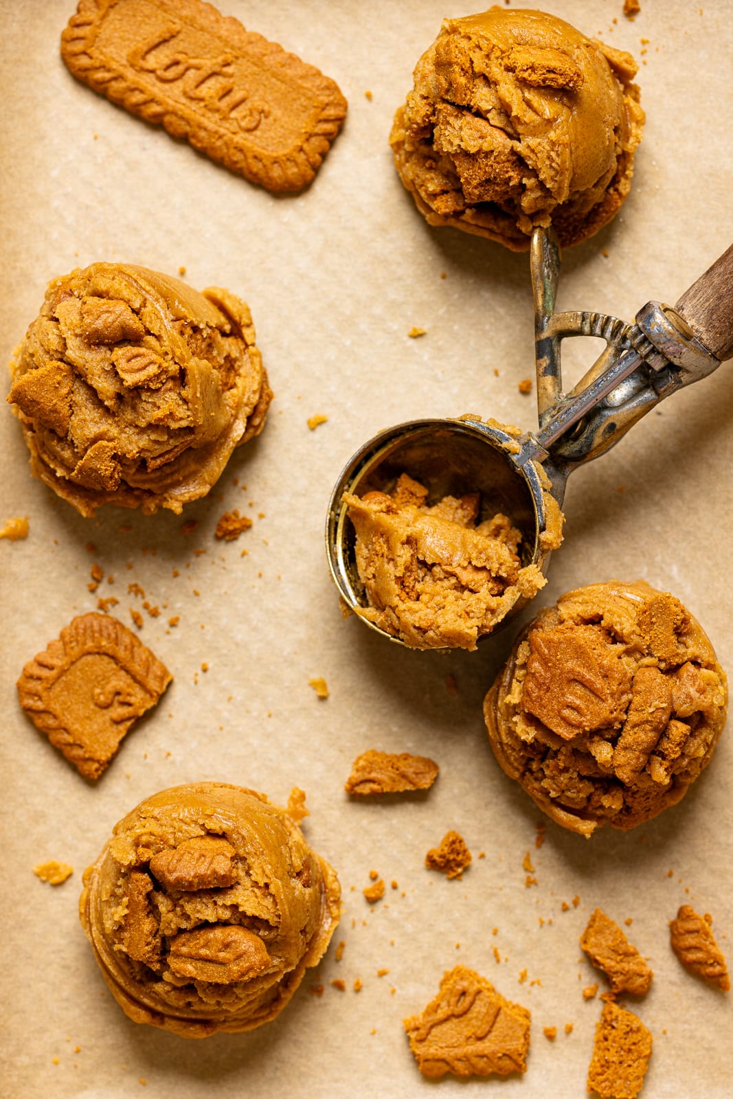 Scooped cookie batter on a baking sheet with parchment paper and cookie scoop.