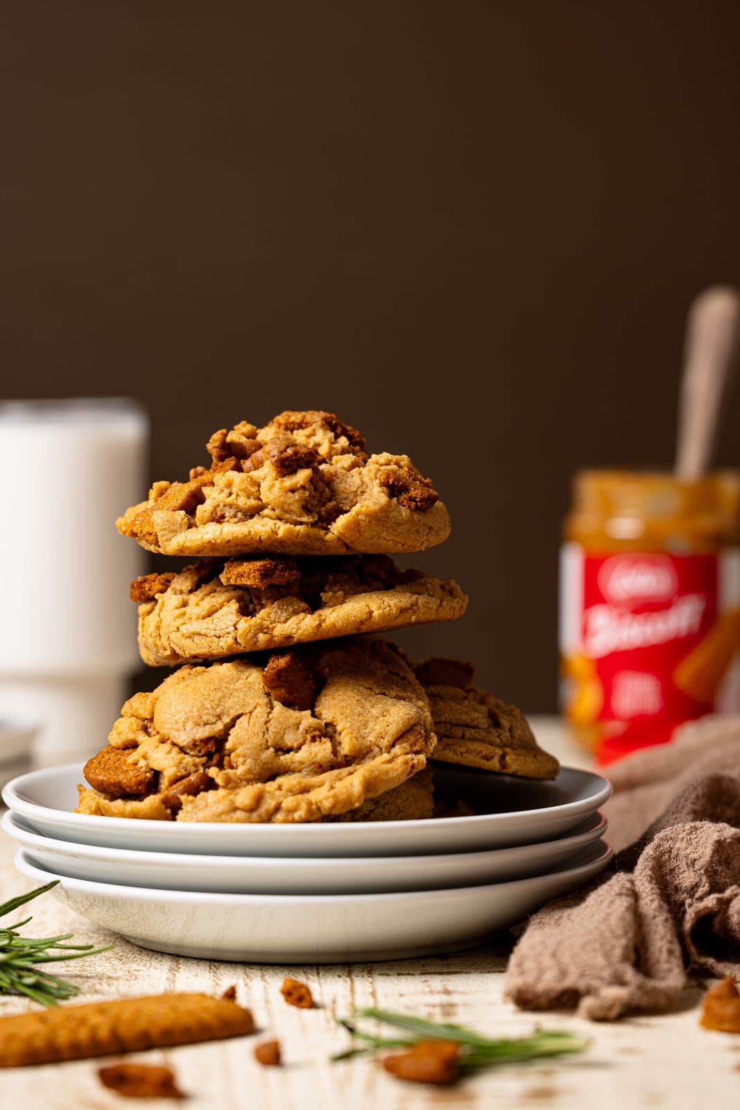 Stack of cookies on three white plates with milk and cookie butter in the background.
