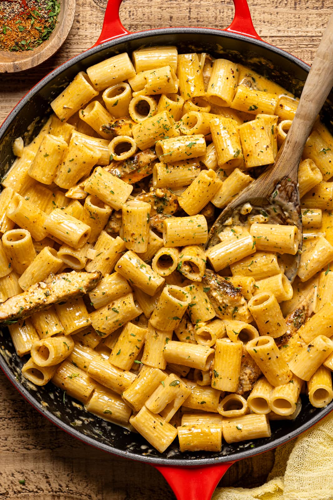 Pasta in a red skillet with a wooden spoon. 