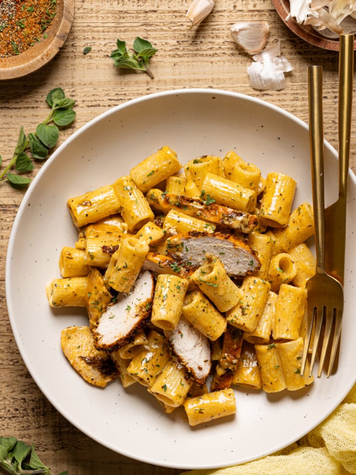 Chicken pasta with a white plate with a knife and fork with garlic and herbs as garnish.